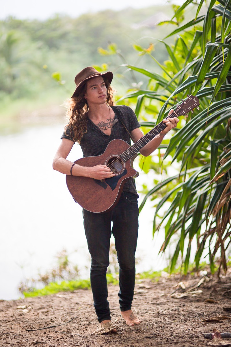 Kauai male model Steven Sedalia playing guitar by the river